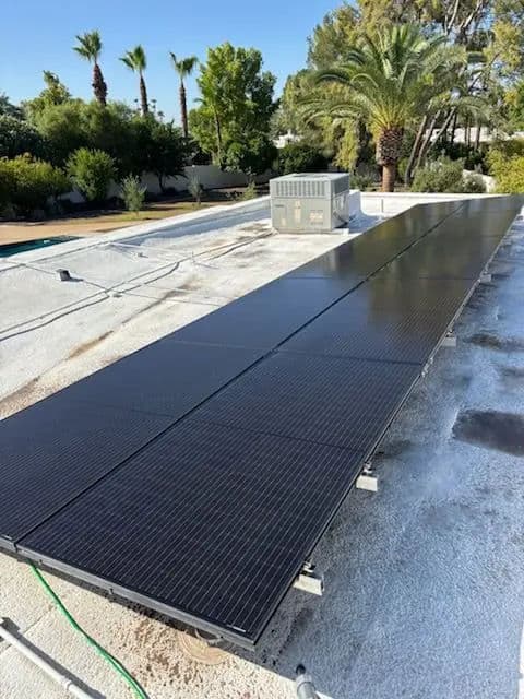 Solar panels installed on a rooftop with palm trees and HVAC unit in the background.