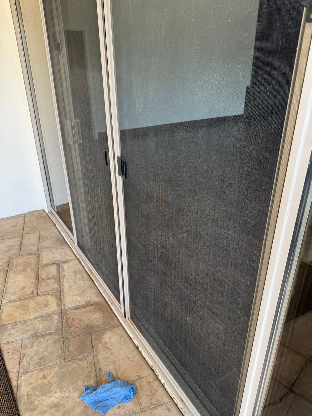 Sliding glass doors with a cleaning cloth on the tiled floor, showing dirt on the glass.