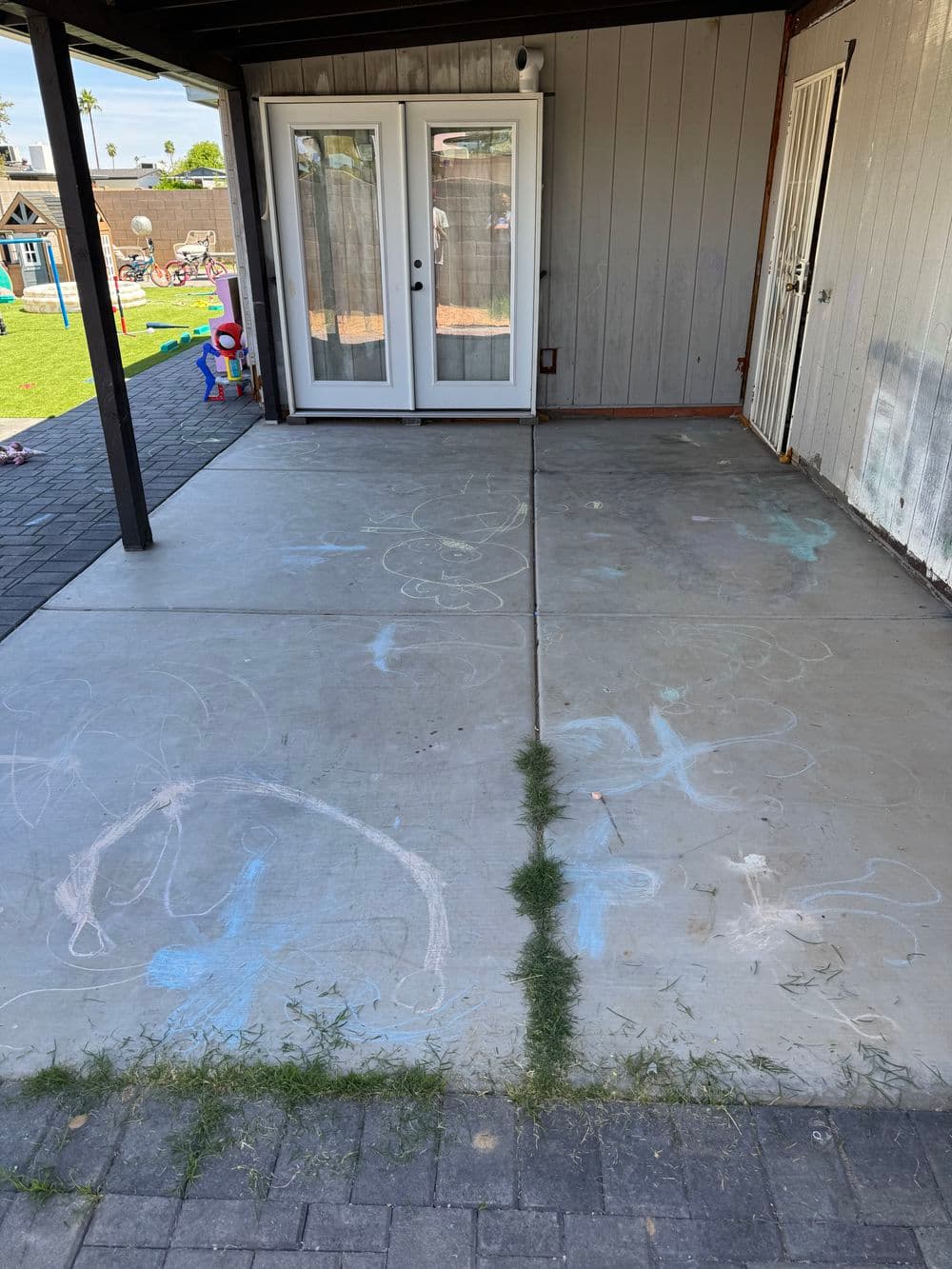 Chalk art on a concrete patio in a backyard with sliding doors and grassy areas.