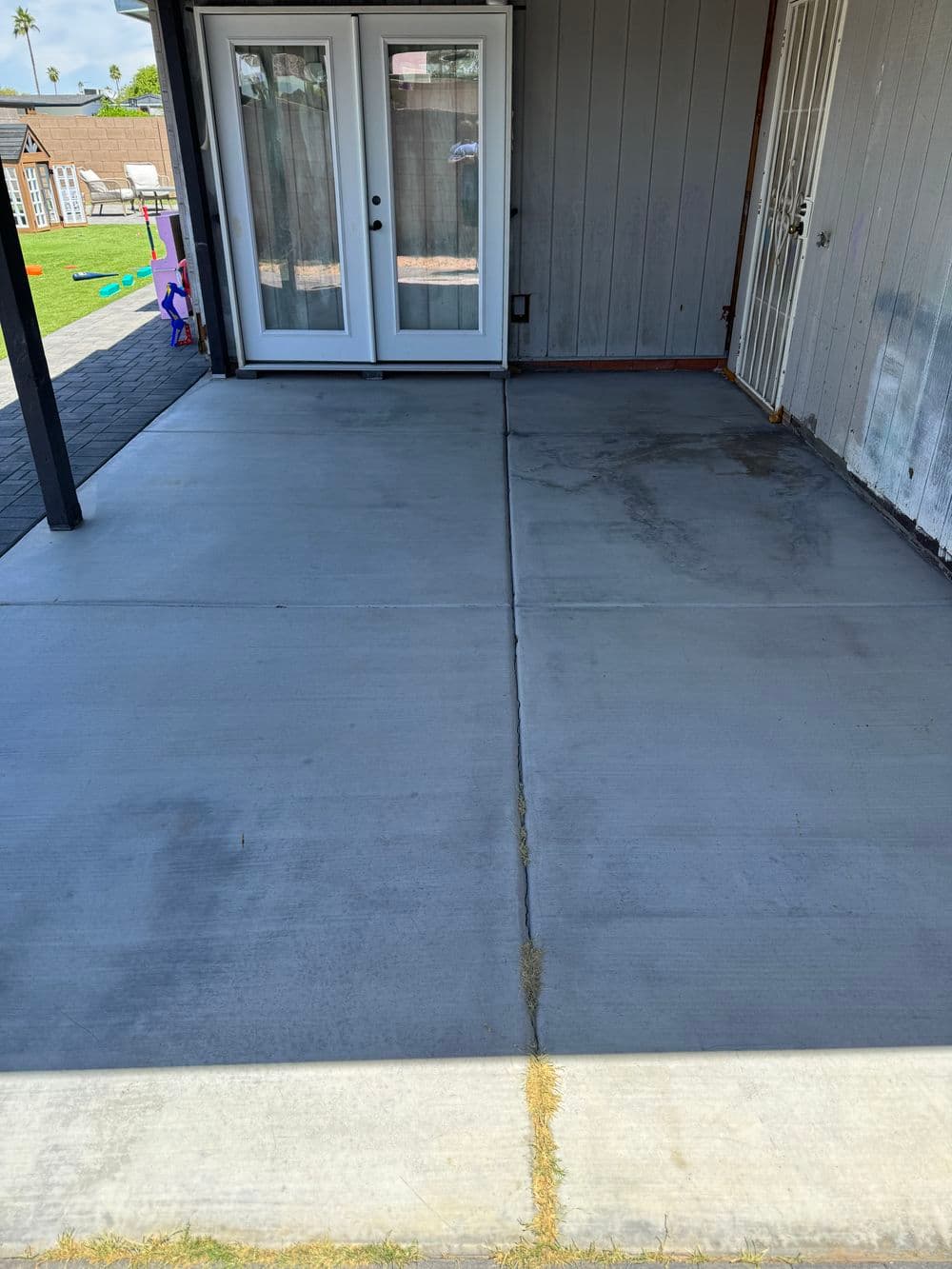 Freshly poured concrete patio with clean lines and adjacent double doors, sunny exterior.